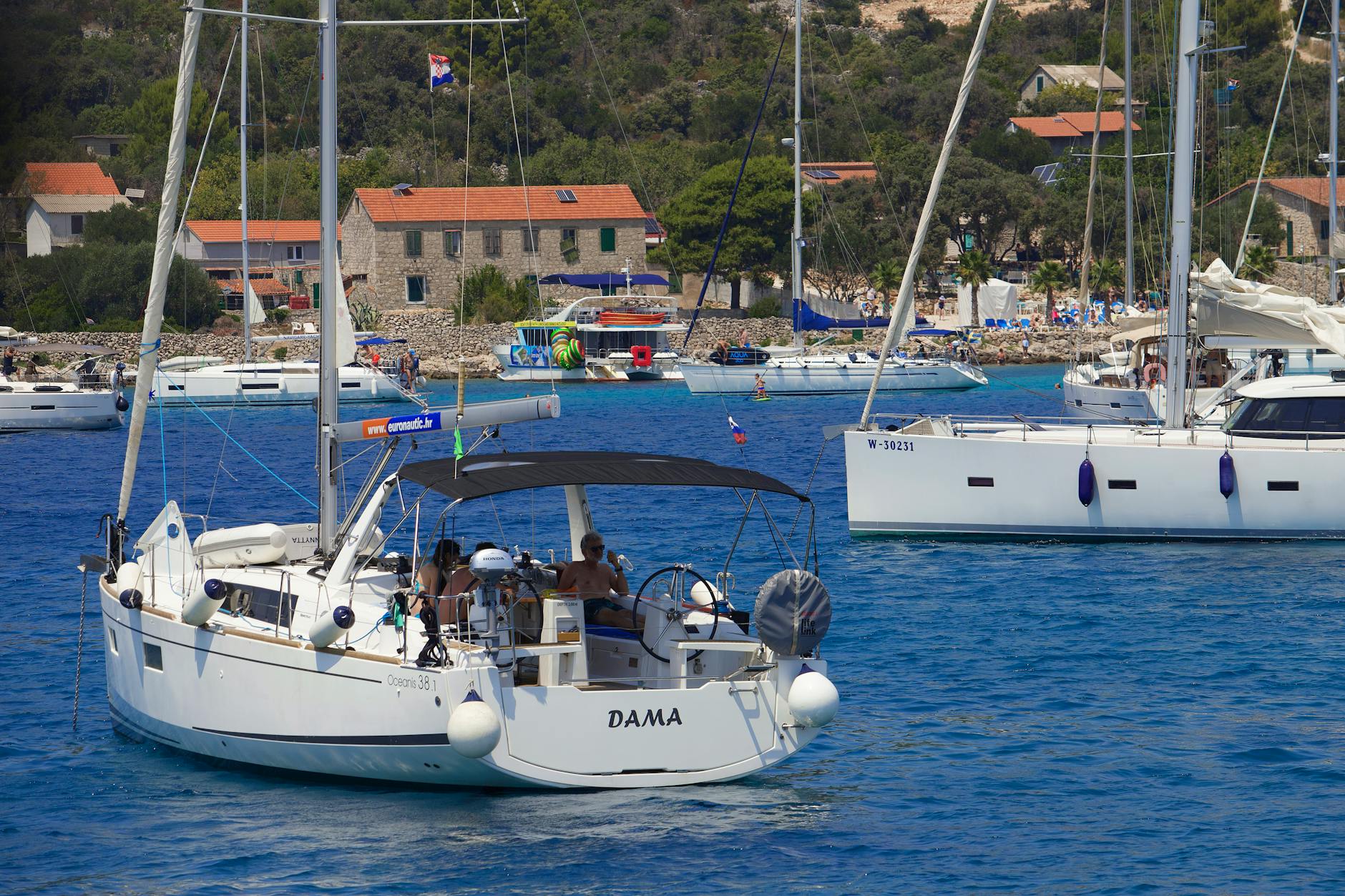 Sailing yachts in a beautiful Mediterranean bay with houses and lush greenery in the background. (Photo: Viktor Färber / Pexels)