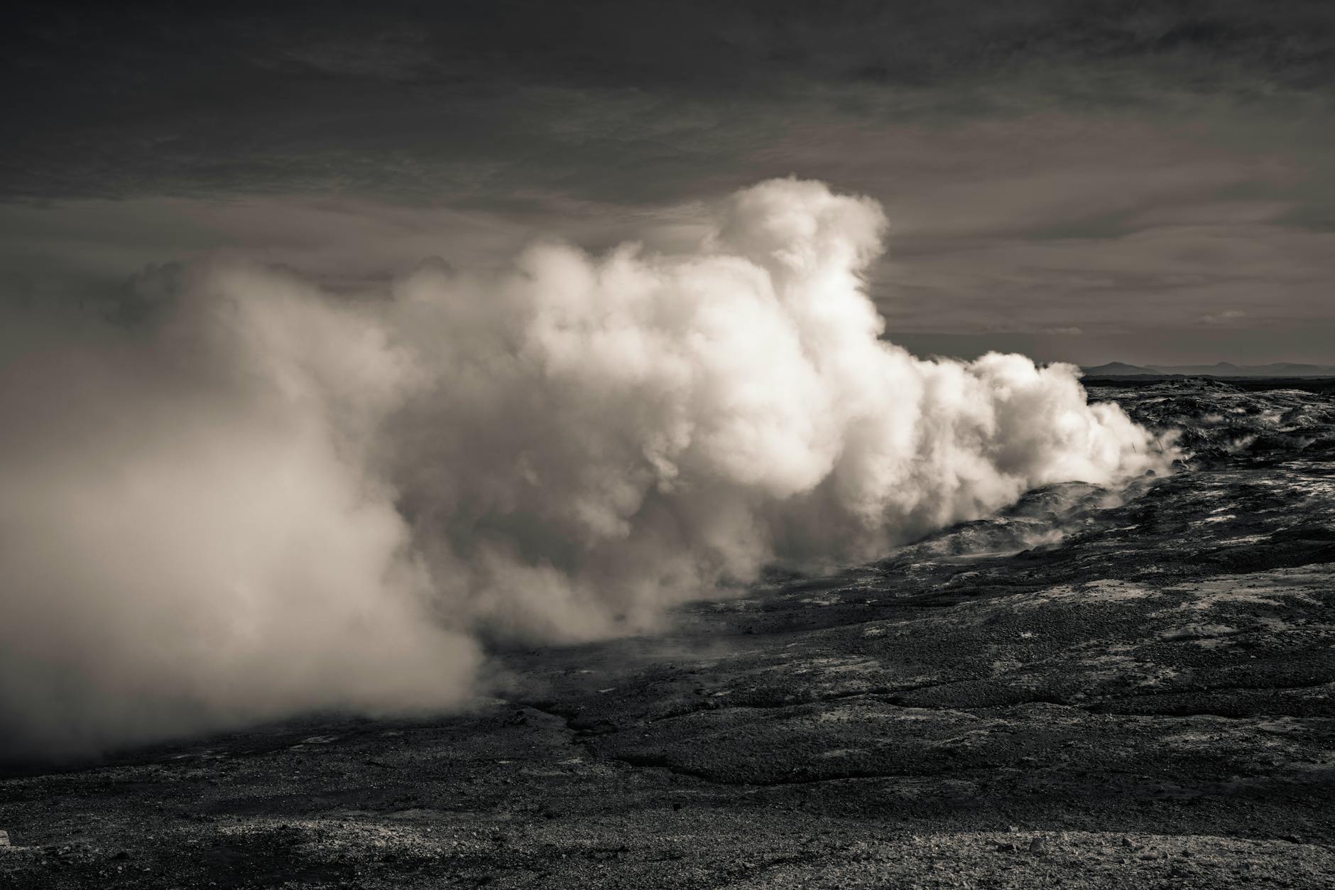 Captivating black and white photo of an Icelandic geyser emitting steam, set against a rugged landscape. (Photo: Raul Ling / Pexels)