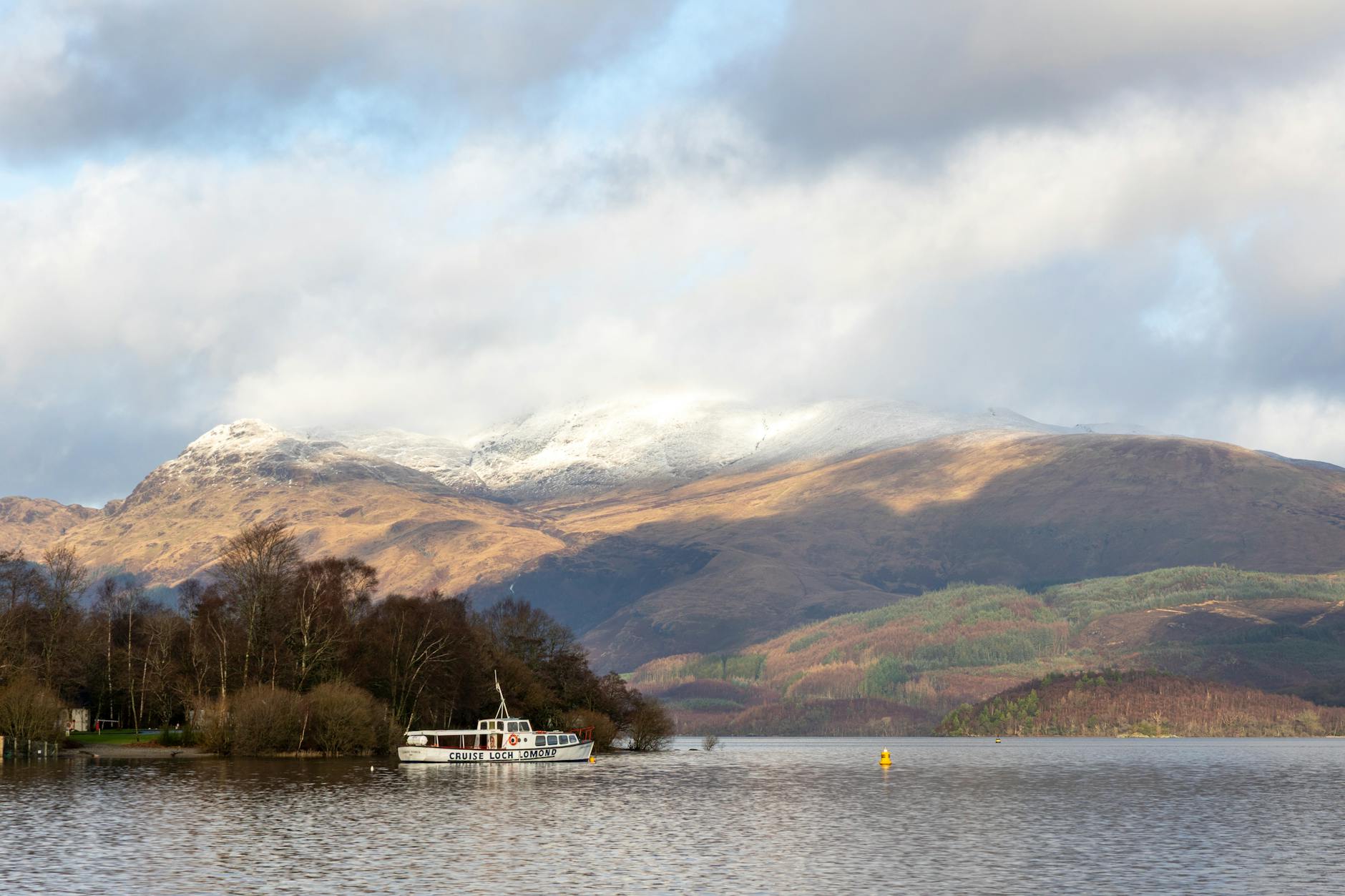 A scenic winter view of Loch Lomond with a boat and snow-capped mountains in Scotland. (Photo: Igor Passchier / Pexels)